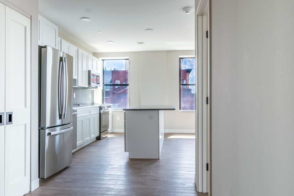 Modern kitchen with white cabinets, stainless steel appliances, a central island, and two large windows letting in natural light. Hardwood floors and neutral walls create a bright, open atmosphere.